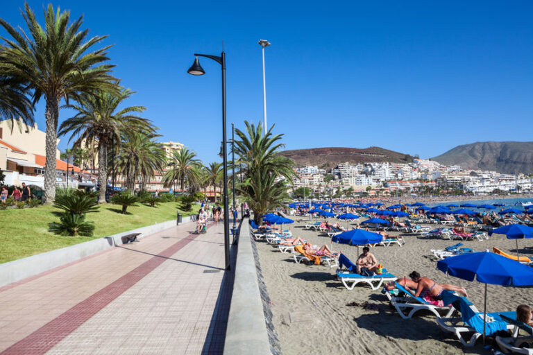LOS CRISTIANOS, TENERIFE, CANARY, SPAIN - CIRCA JAN, 2016: Pathway is along Famouse urban beaches with fine sand. Blue parasols and sunbeds are on coastline. The Atlantic ocean